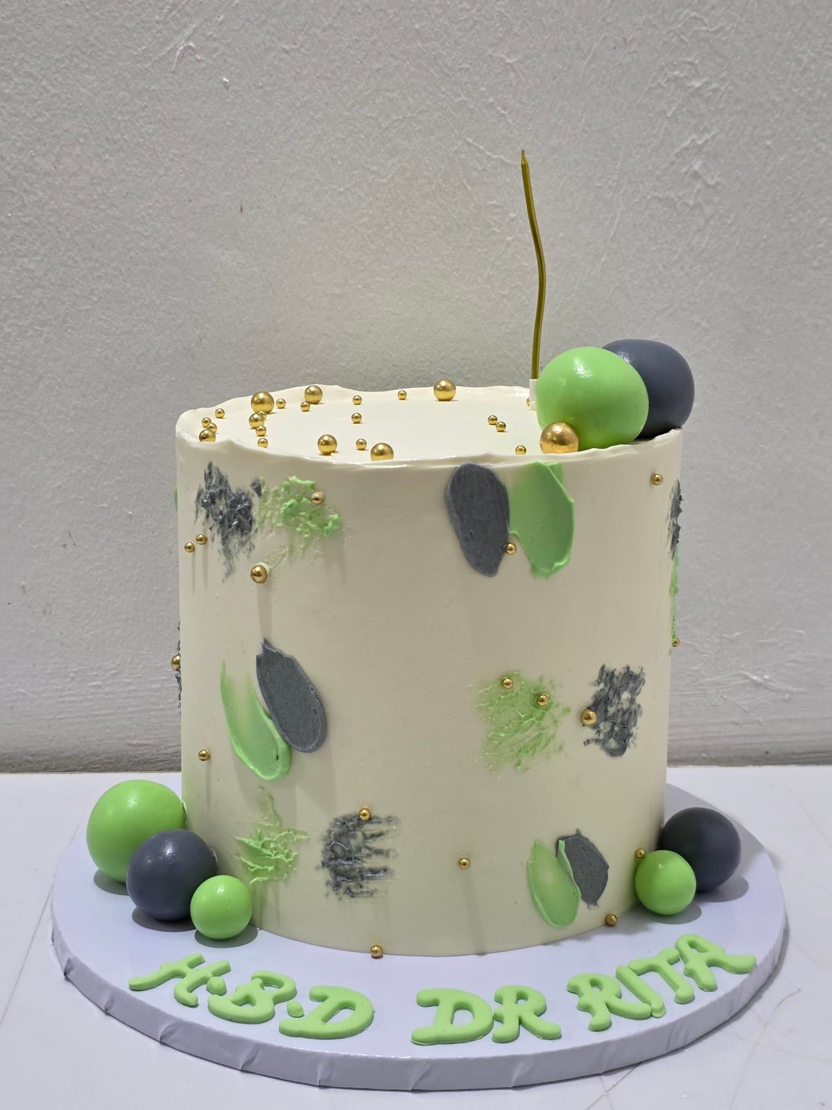 Tall cream cake with abstract green and charcoal brushstrokes, gold beads, green and grey spheres, and a fine gold wire detail on top