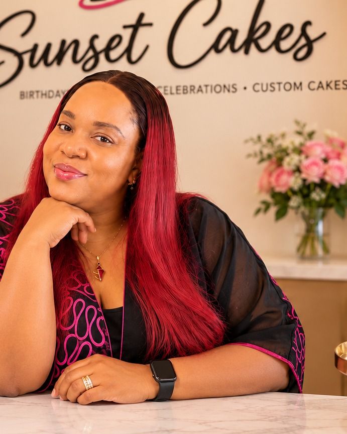Mrs. Chinonye Odagwe, founder and baker at Sunset Cakes, resting her chin on her hand at a marble counter in front of the Sunset Cakes sign