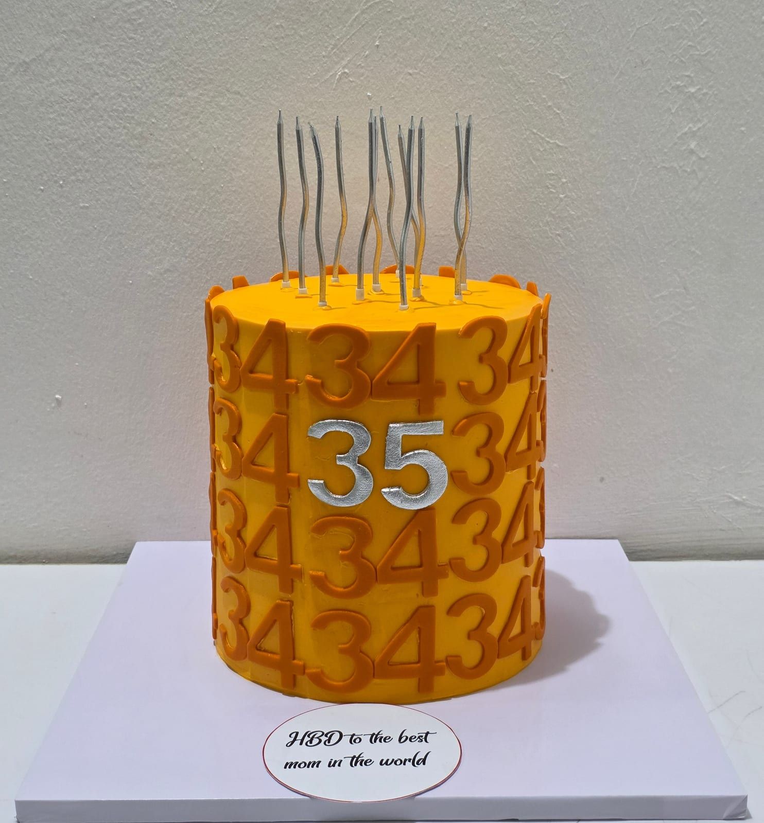 Tall orange cake embossed with a repeating raised number pattern, topped with a silver numeral and slim silver candles