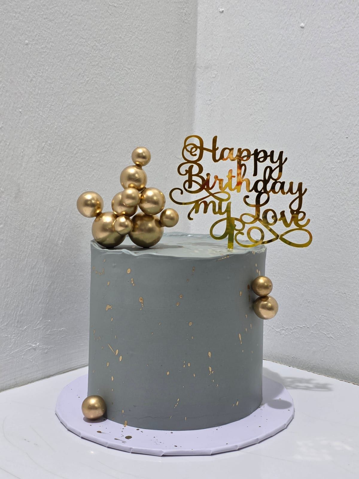 Tall grey cake with fine gold marbling, a cluster of gold spheres on top and a gold script topper