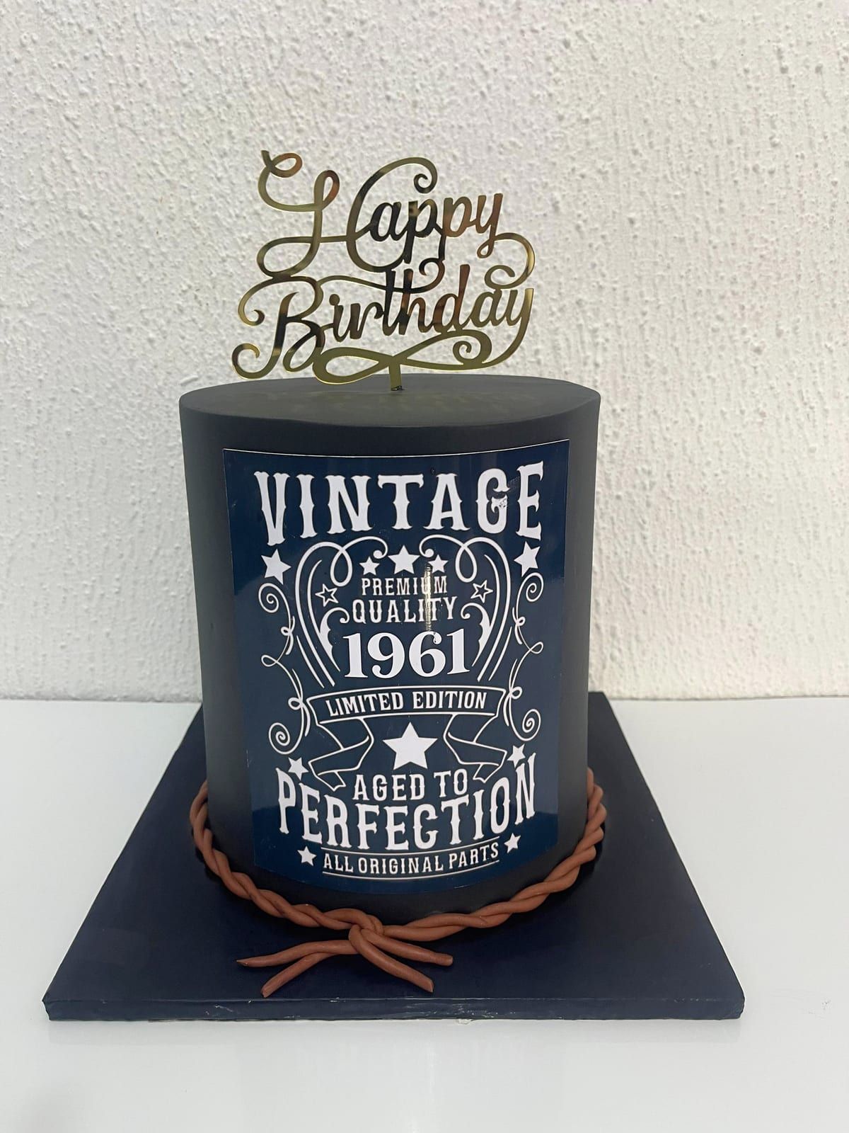 Tall charcoal cake printed with a white vintage-style label reading Aged To Perfection, finished with a piped rope trim at the base